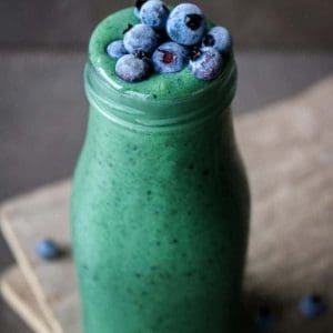 Glowing Green Spirulina Smoothie in a glass with blueberries on top