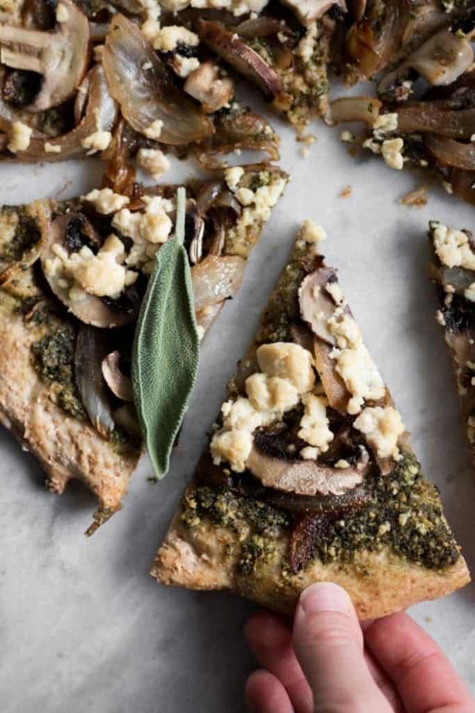 hand taking slice of pizza with sage pesto