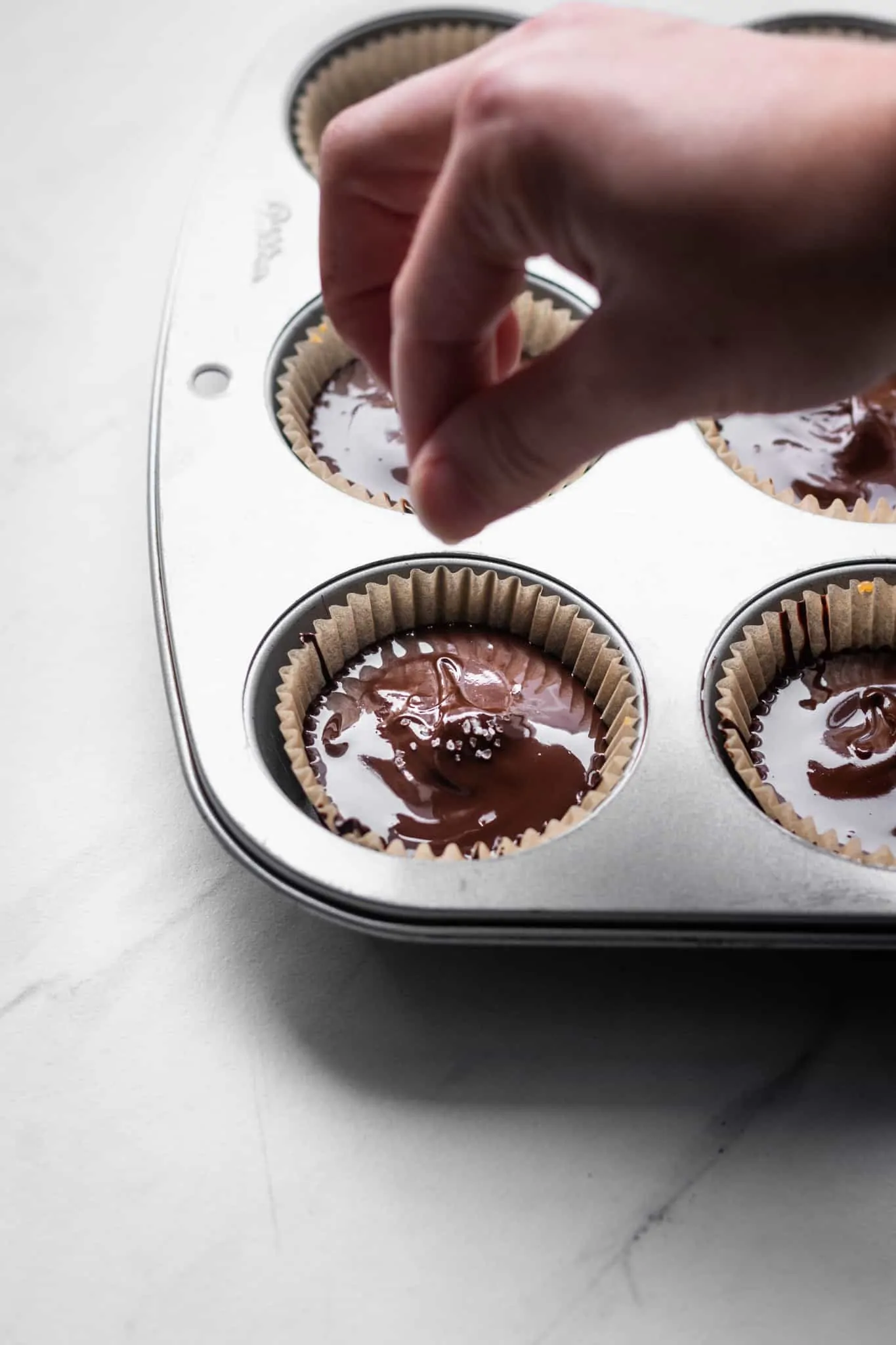 hand sprinkling sea salt over chocolate cups